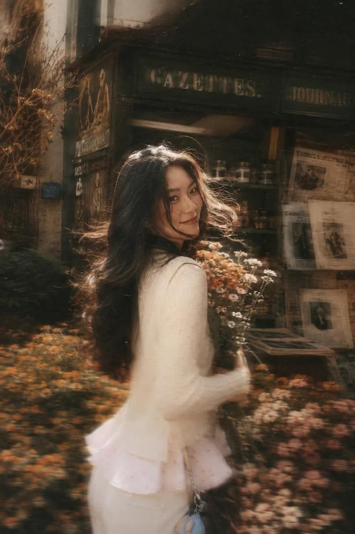 A beautiful young woman with long dark flowing hair holding a bouquet of soft pink roses, tur…